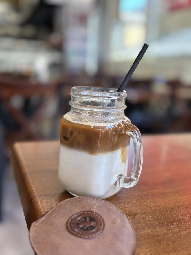 An iced latte in a mason jar with the cafe blurred behind